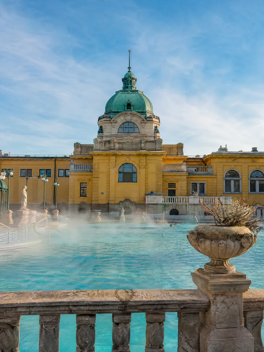 Das Thermal-Außenbecken des Széchenyi-Bads mit aufsteigendem Dampf vor den gelben neobarocken Flügeln